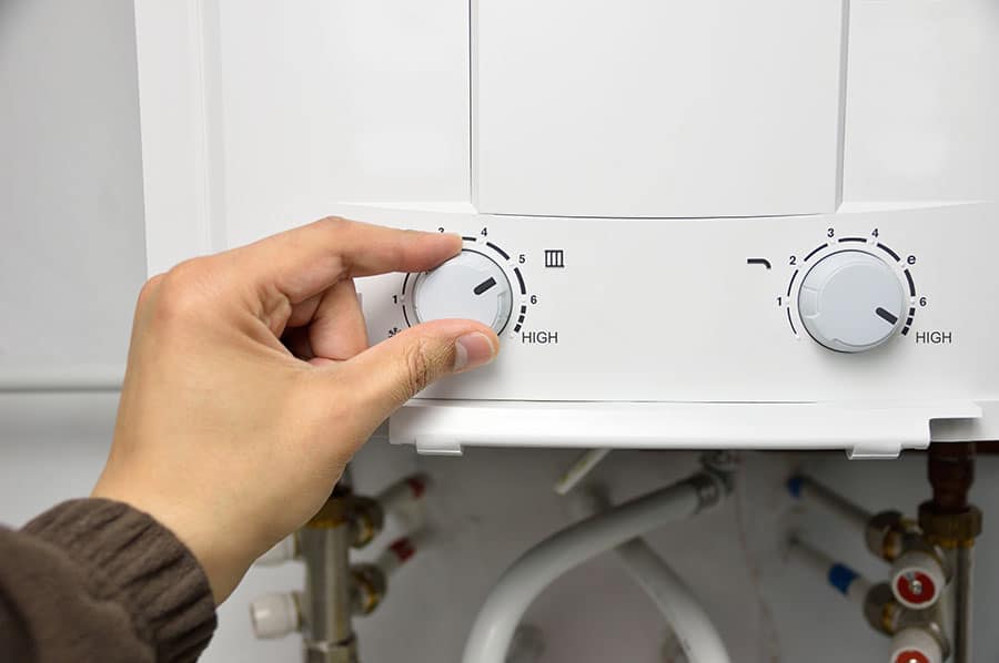 A person adjusting the hot water temperature on a bathroom’s water heater, highlighting the importance of choosing a safe and reliable water heater for the home.