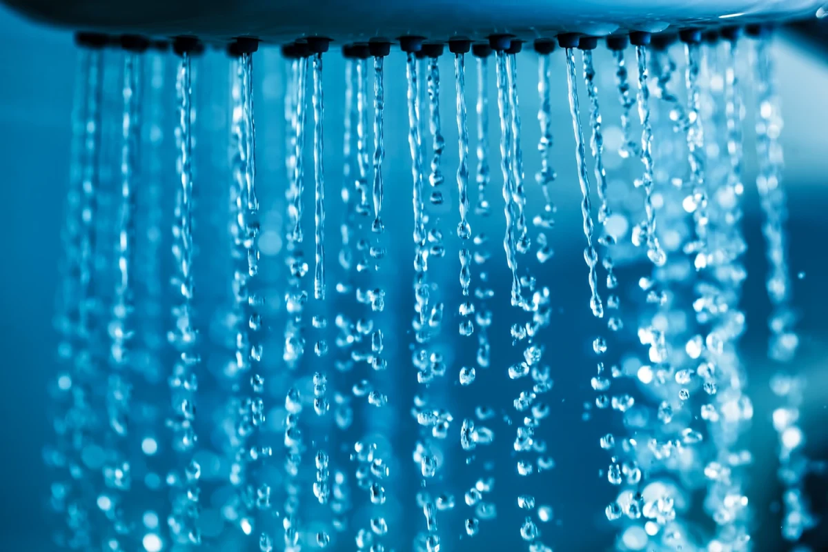 Close-up of a shower head with water flowing, showing on-demand hot water supply